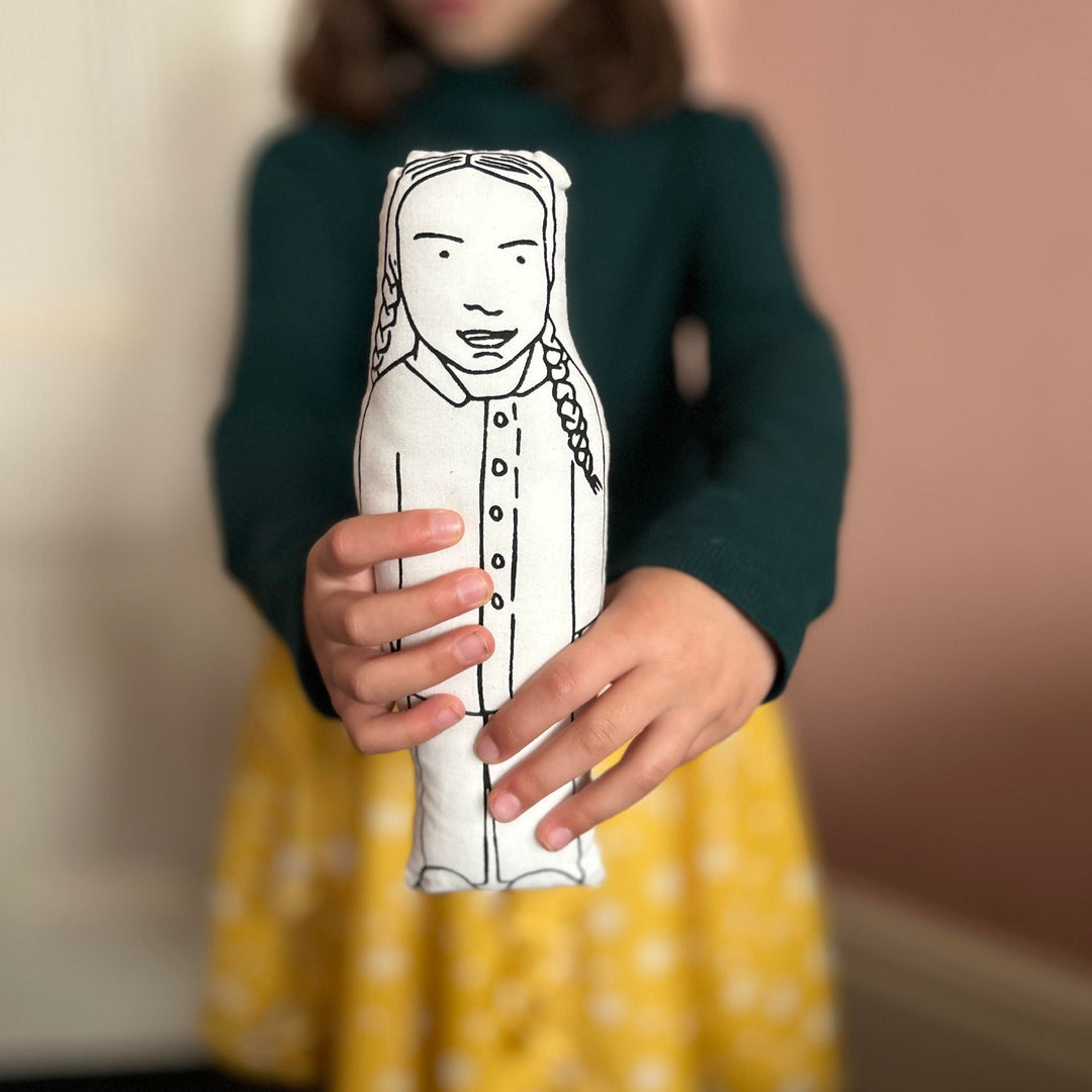 A child holding out screen printed doll cushion of climate activist Greta Thunberg towards the camera