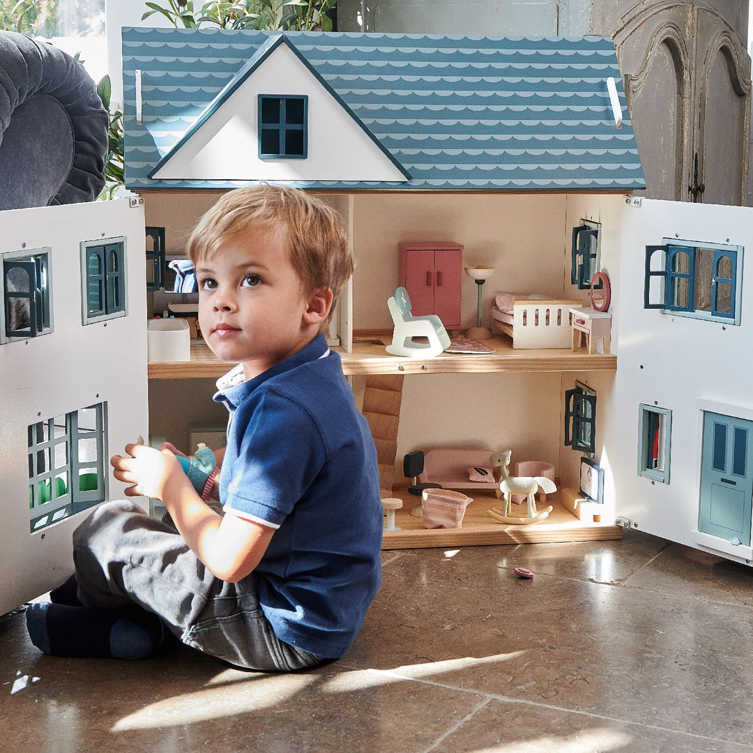Child playing with a dollhouse set up with furniture and accessories.