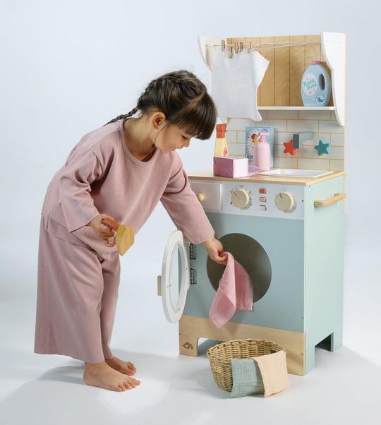 Child playing with a toy washing machine and dryer set on a light grey background