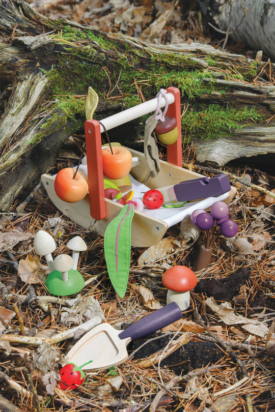 Miniature garden set with a wooden bench, fruits, vegetables, and gardening tools on a natural background.