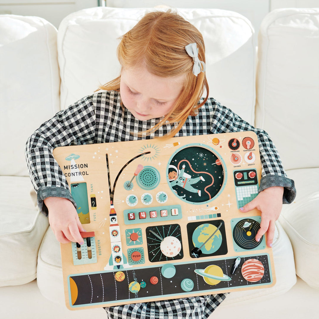 Child holding a space-themed wooden toy on a white couch