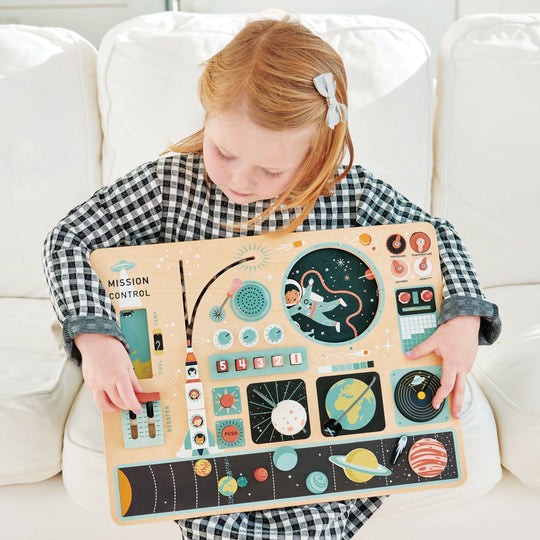 Child holding a space-themed wooden toy on a white couch