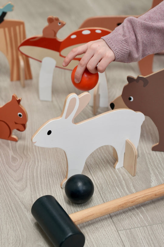 Wooden toy with animal figures and a hand interacting with it on a wooden surface.