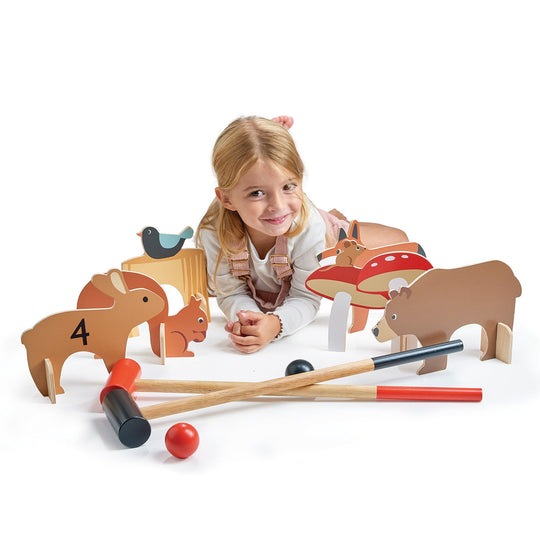 Child playing with wooden animal toys and croquet set on a white background