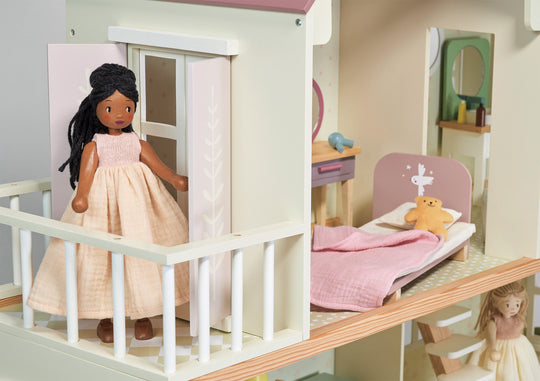Dollhouse with a doll in a pink dress standing inside, surrounded by furniture and toys.