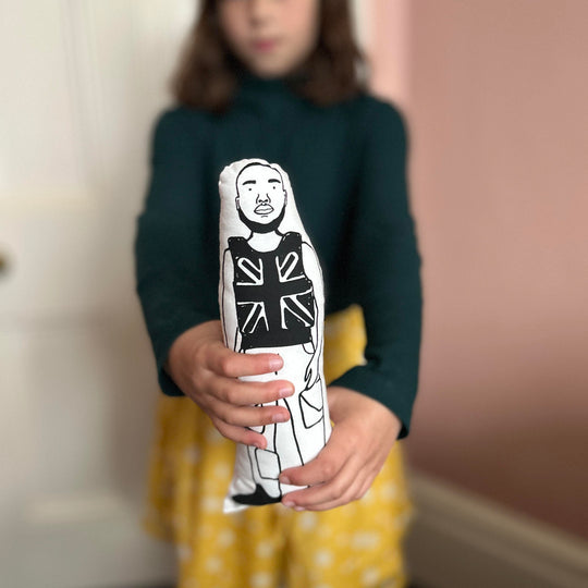 A child holding a black and white screen printed cushion doll featuring an illustration of Stormzy wearing a Union Jack vest