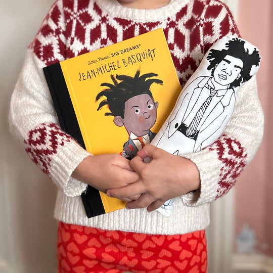 A child holding a screen printed doll cushion and a Little Peopl Big Dreams book about Jean Michel Basquiat's life