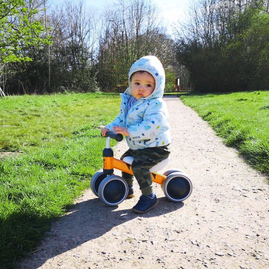Child riding a balance bike on a path with green grass and trees in the background