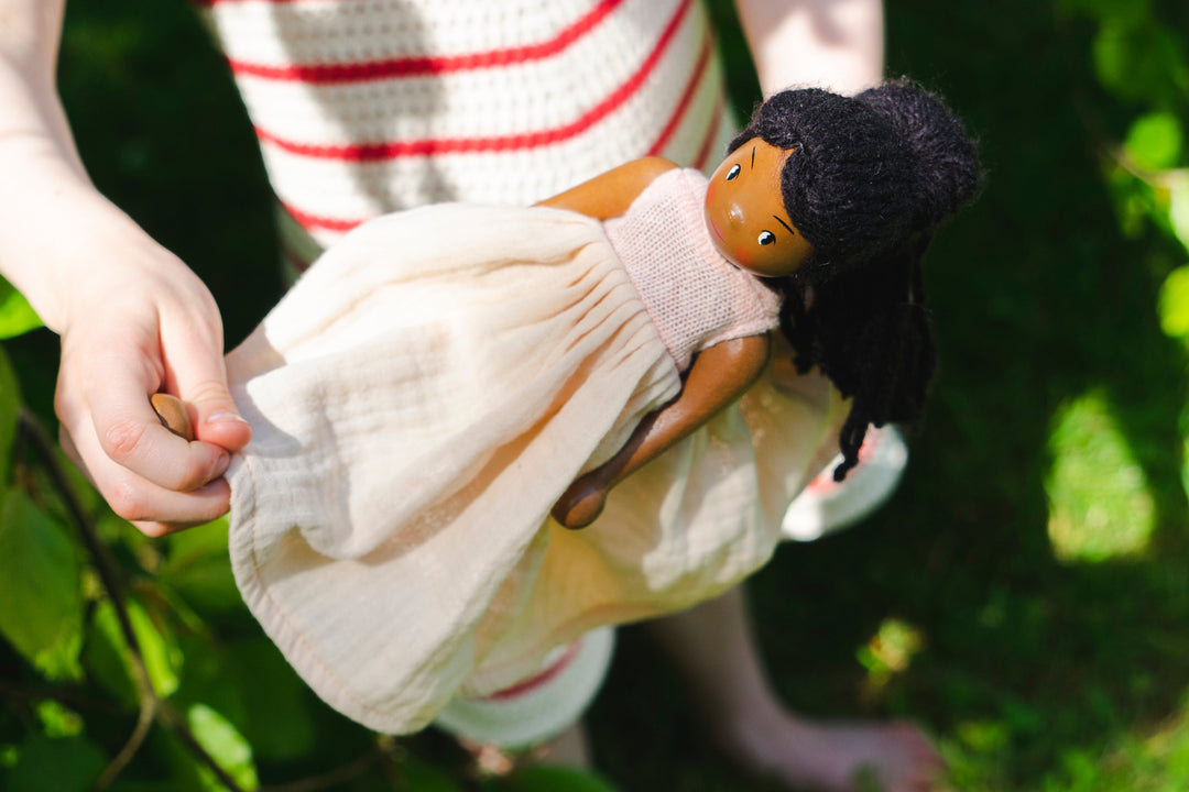 Child holding a doll with a pink dress and black hair, standing outdoors.
