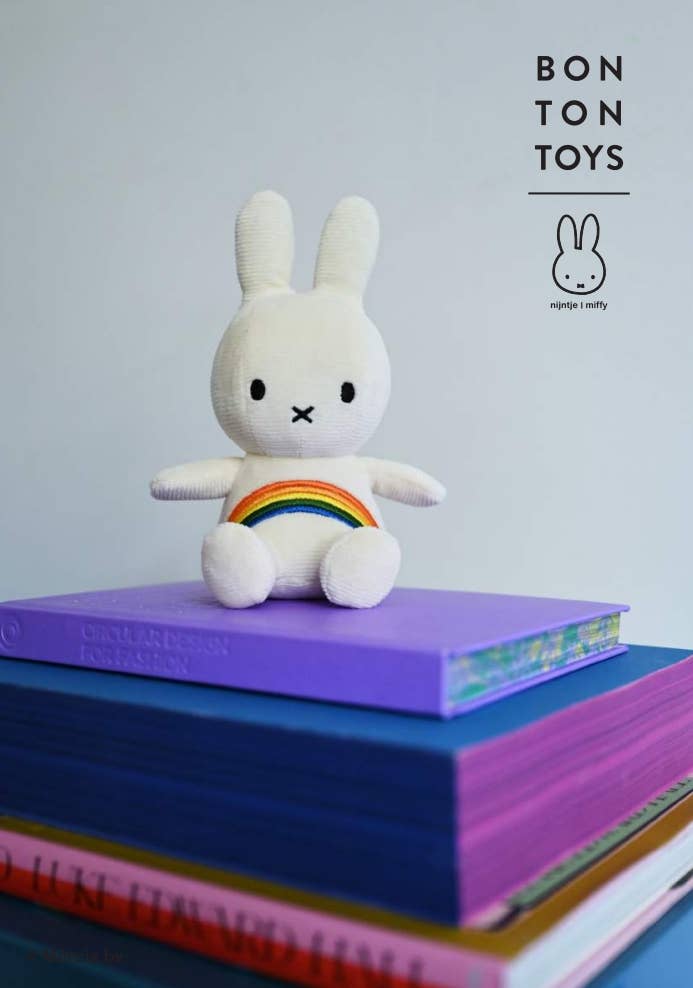 White plush toy with a rainbow on a stack of books, featuring the Bon Ton Toys brand.