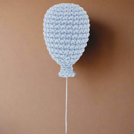 A baby blue handmade crochet balloon with a string attachment, displayed against a wall background.