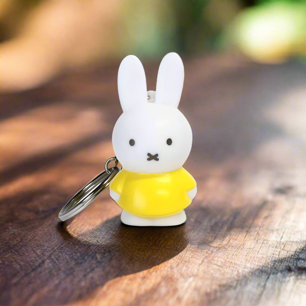 Keyring with a cartoon Miffy character with iconic cross stitched mouth wearing a yellow dress on a white background