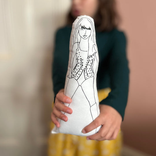 A child holding out the screen printed doll of Taylor Swift towards the camera with a blurred background