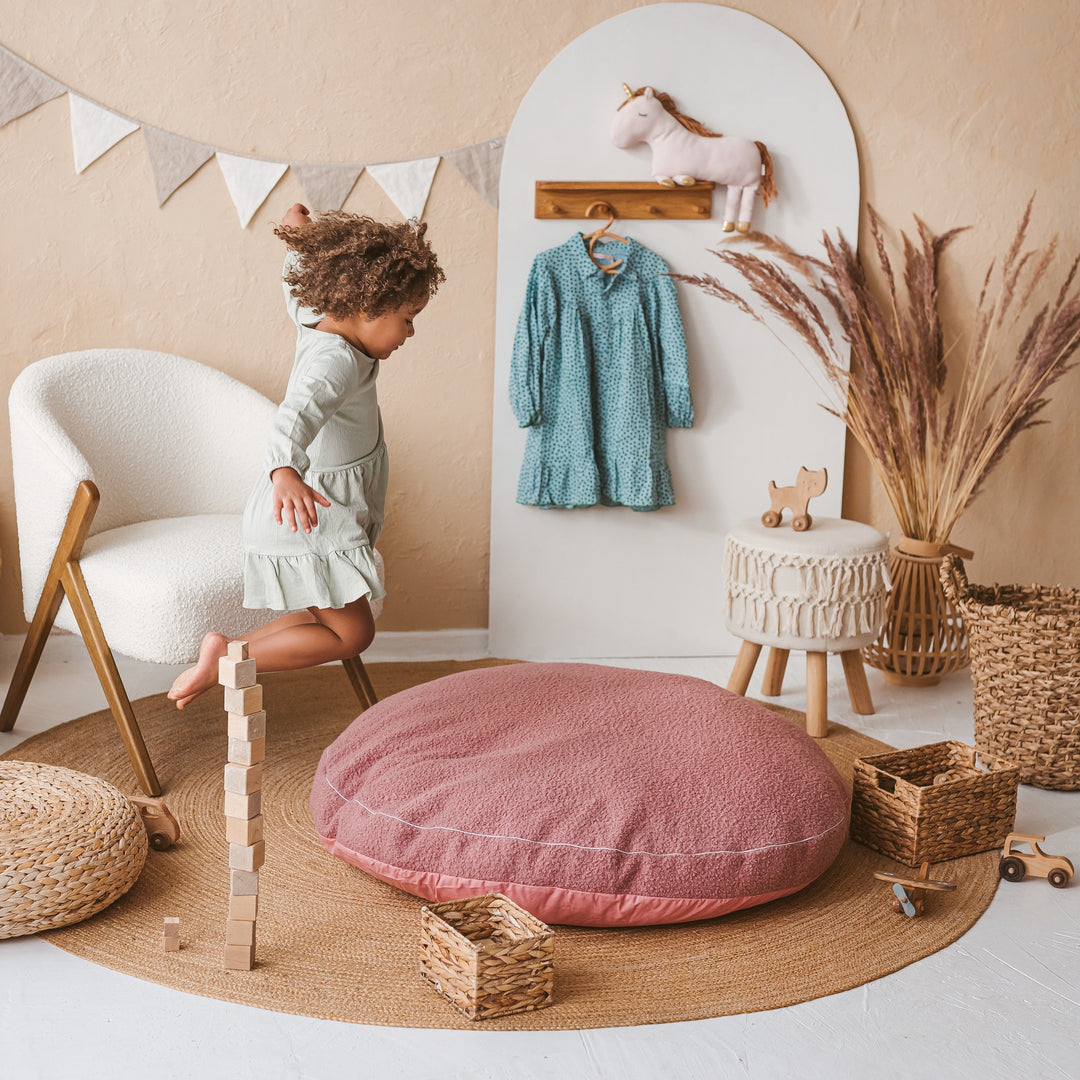 Child playing in a playroom with a pink cushion, wooden blocks, and a white chair.