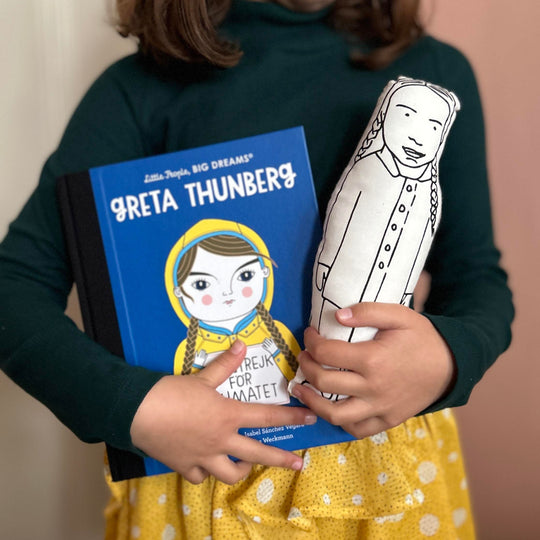A child holding a screen printed doll of Greta Thunberg and a Little People Big Dreams book about Geta Thunberg's life