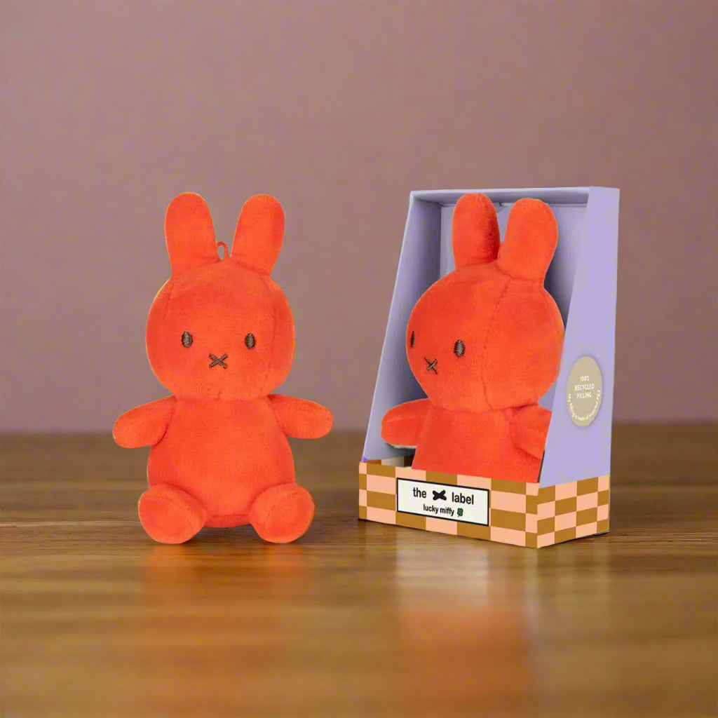 Bright coral orange stuffed toy rabbit with iconic cross stitched mouth in purple gift box