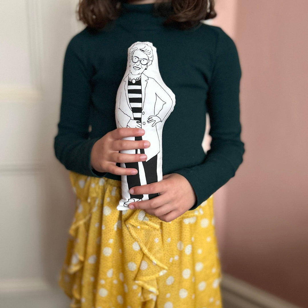 A child holding a black and white screen printed cushion doll depicting Prue Leith, suitable for fans of the Great British Bake Off
