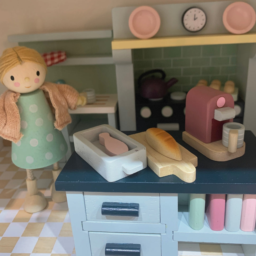 Toy kitchen set with a doll and various kitchen items on a checkered floor.