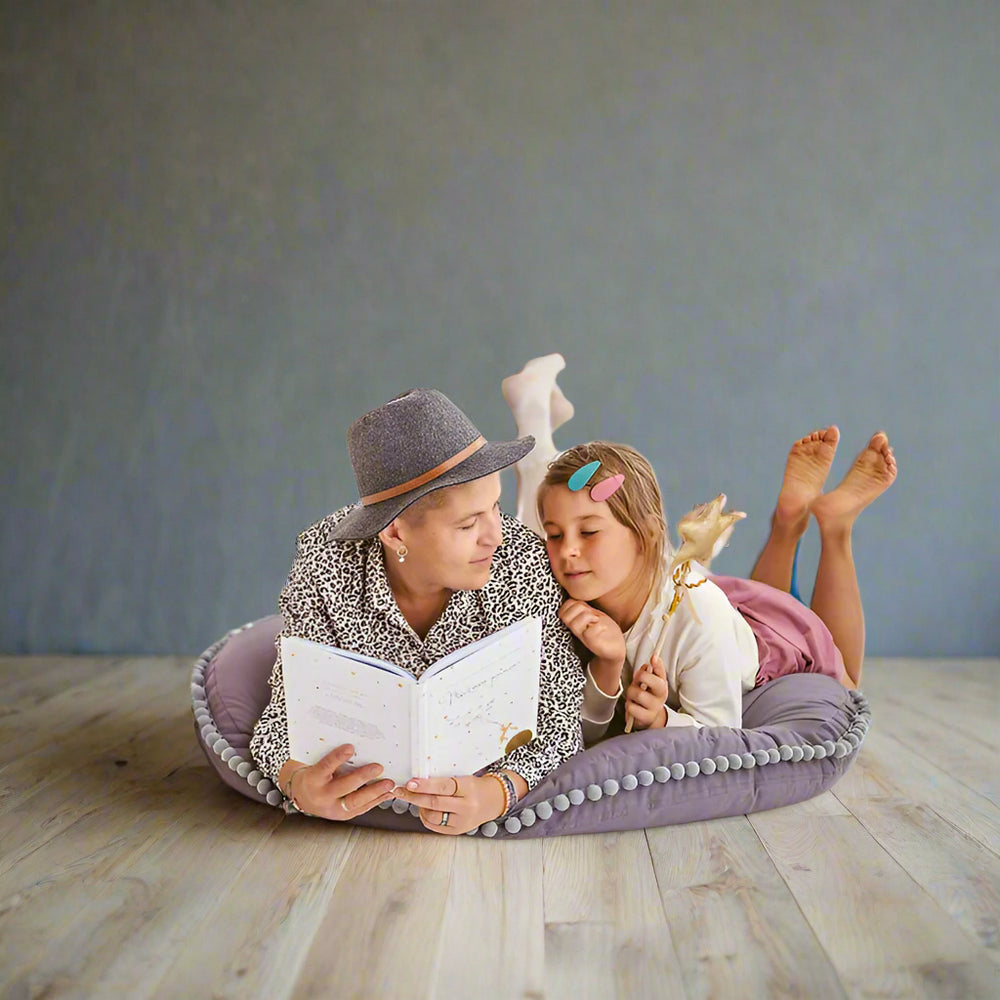 Woman and child lying on a grey floor cushion reading a book