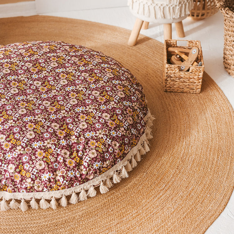 Close up of round floor cushion, showing a beautiful retro 70s-style floral pattern with a burgundy background, and cream trim with tassels