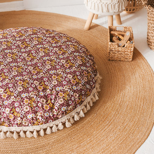 Close up of round floor cushion, showing a beautiful retro 70s-style floral pattern with a burgundy background, and cream trim with tassels