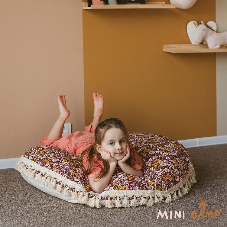 Child lying on a floral-patterned cushion against a wall with shelves.