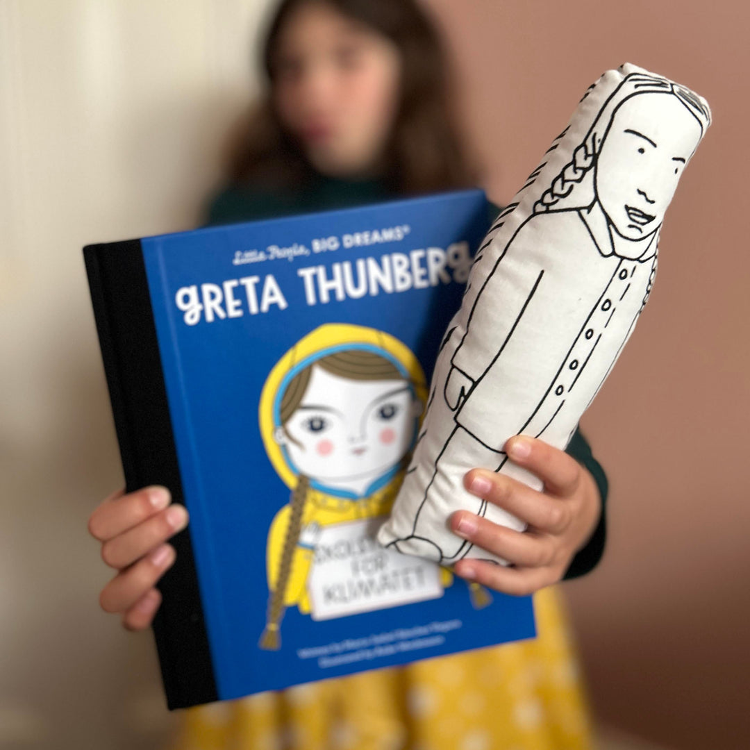 A child holding a screen printed cushion doll depicting climate activist Greta Thunberg, with a book of Greta Thunberg's illustrations in the background.