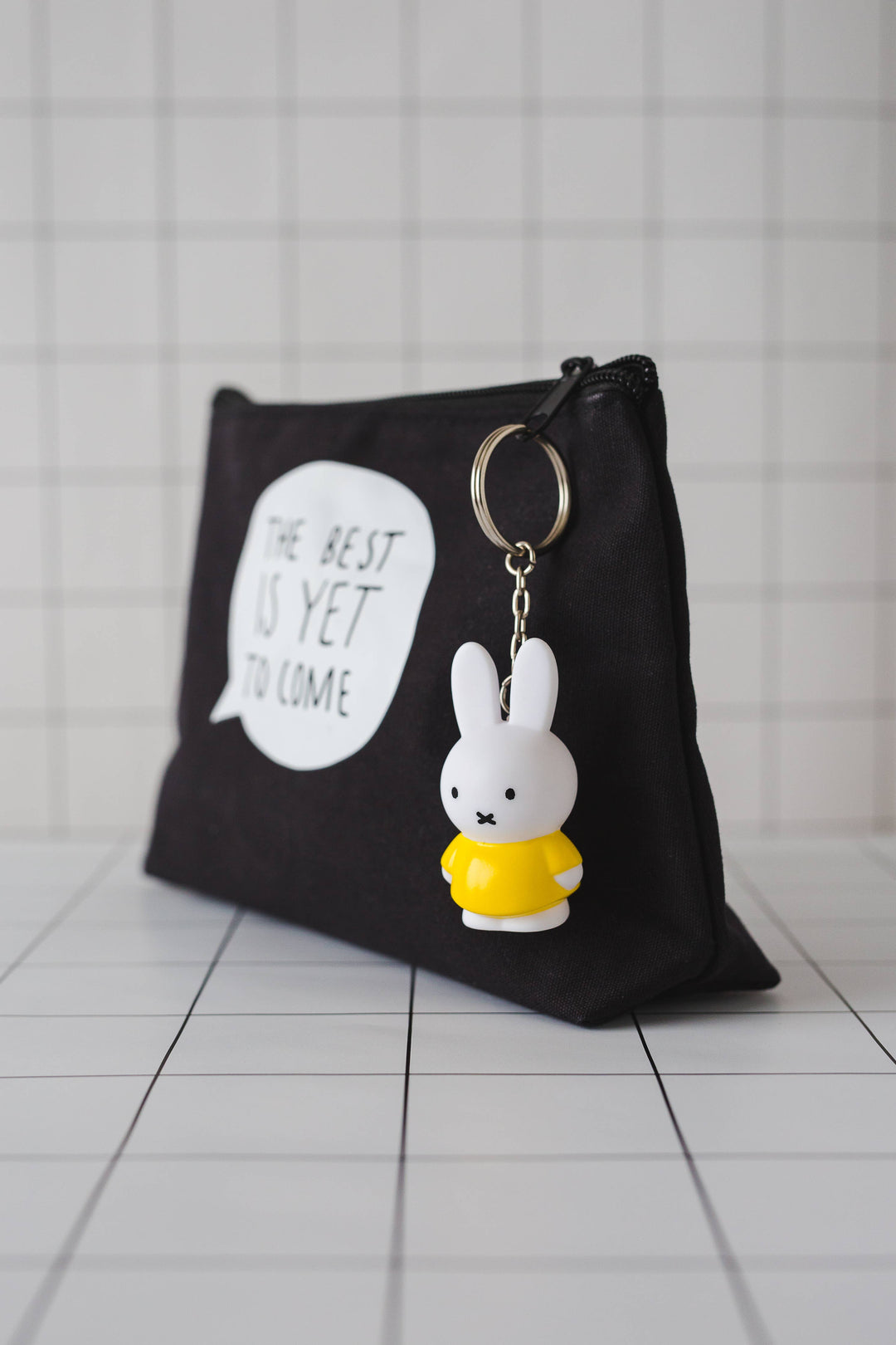 Black wash bag with a keyring of a white rabbit wearing a yellow dress attached to the zip