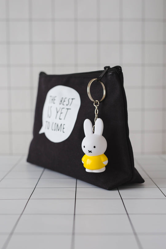 Black wash bag with a keyring of a white rabbit wearing a yellow dress attached to the zip