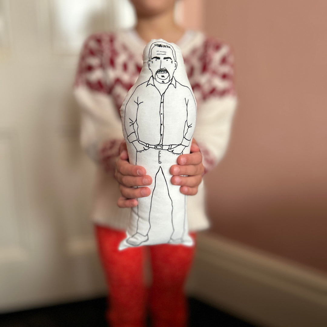 A child holding out the screen printed doll cushion of Paul Hollywood