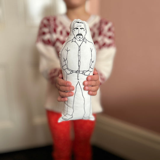 A child holding out the screen printed doll cushion of Paul Hollywood