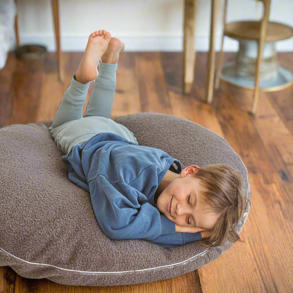 Child lying on large round grey floor cushion