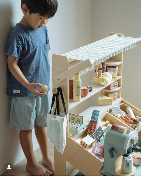 Child playing with a wooden toy kitchen set against a plain wall.
