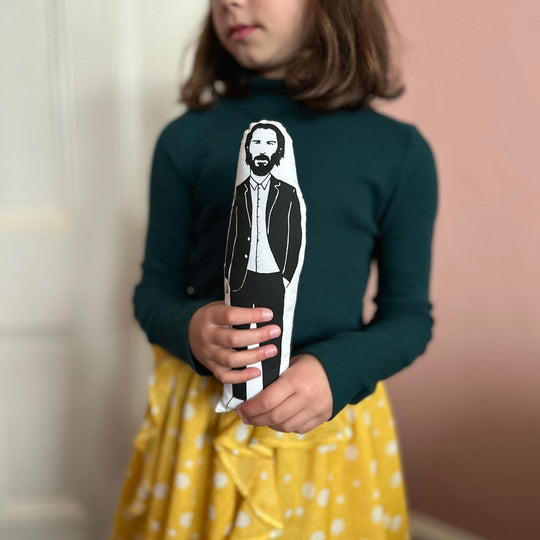 A child holding a screen printed doll cushion of Keanu Reeves