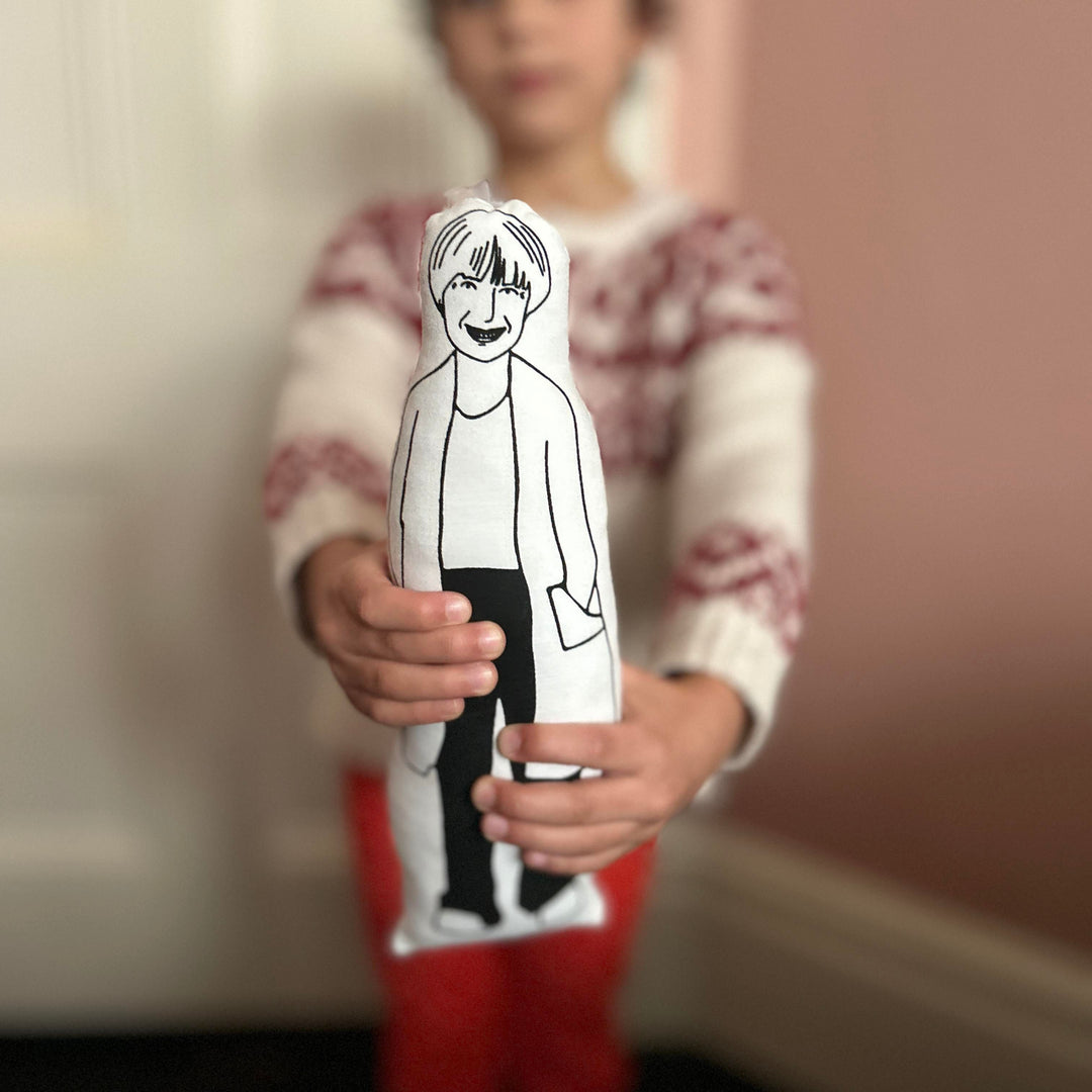 A child holding a black and white screen printed cushion doll with an illustrated design of Victoria Wood