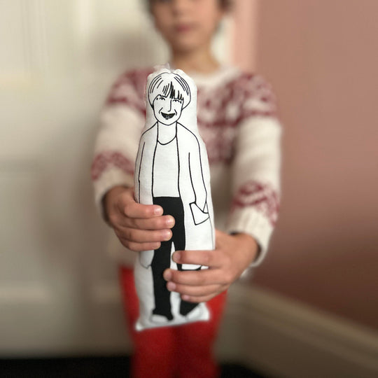 A child holding a black and white screen printed cushion doll with an illustrated design of Victoria Wood