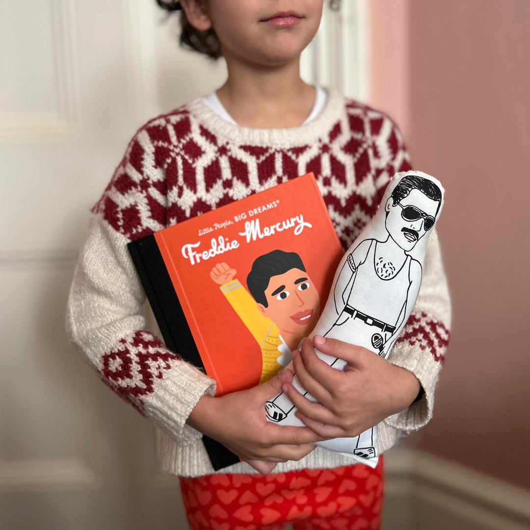 A child holding a screen printed doll of Freddie Mercury and a Little People Big Dreams book about Freddie Mercury's life