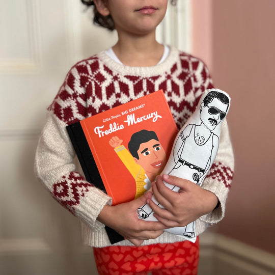 A child holding a screen printed doll of Freddie Mercury and a Little People Big Dreams book about Freddie Mercury's life