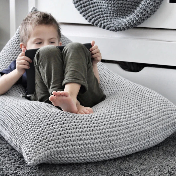 Child reading while sat on a handknitted beanbag in a light grey colour