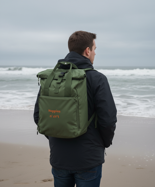 Person wearing a green backpack with 'Nappies n' Sh*t' text on a beach.