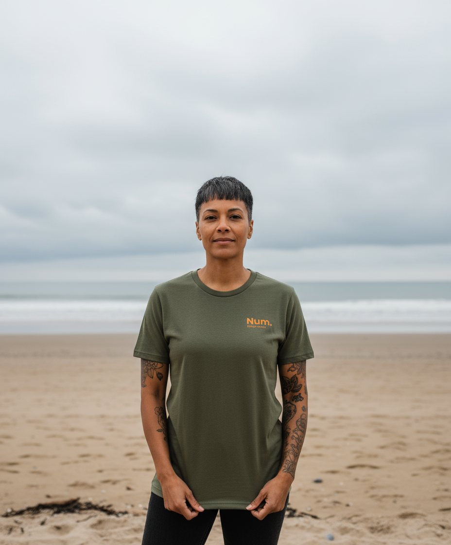 Person wearing a green t-shirt with 'Num' logo on a beach