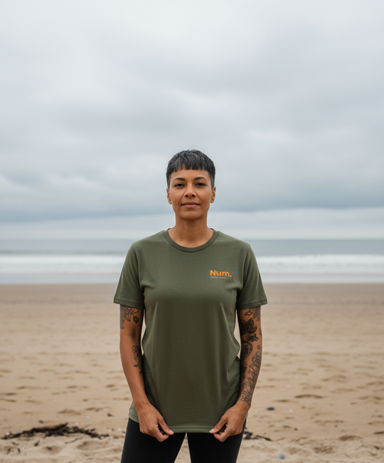 Person wearing a green t-shirt with 'Num' logo on a beach