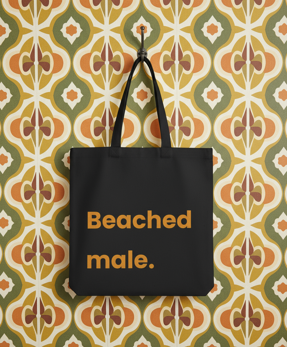 Black tote bag with 'Beached male.' text on a patterned wall background
