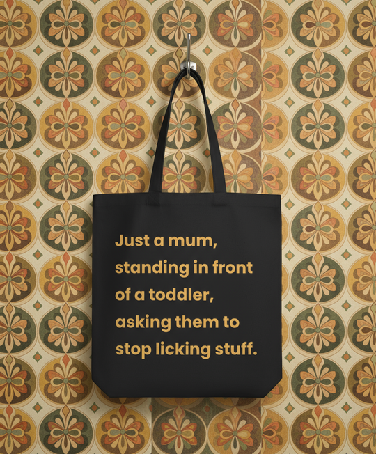 Black tote bag with yellow text on a patterned wall background