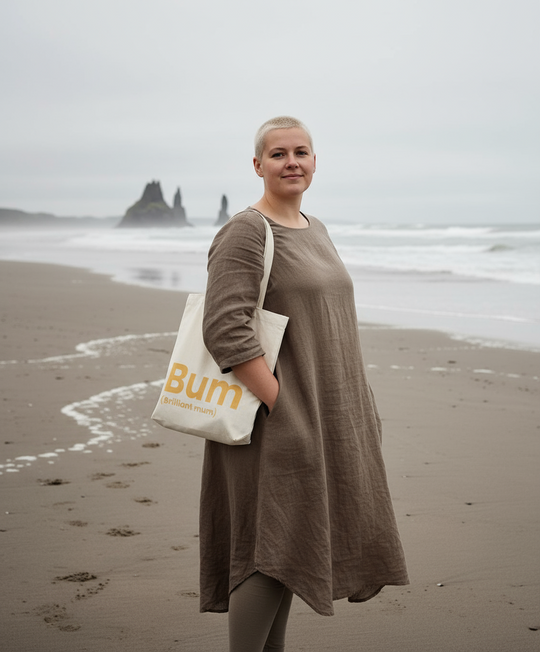 Woman holding a tote bag with 'Bum' printed on it on a beach.