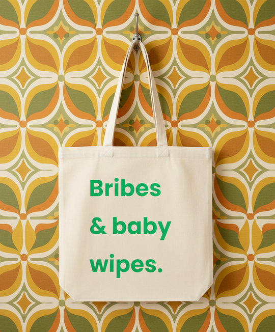 Tote bag with 'Bribes & baby wipes.' text against a patterned wall.