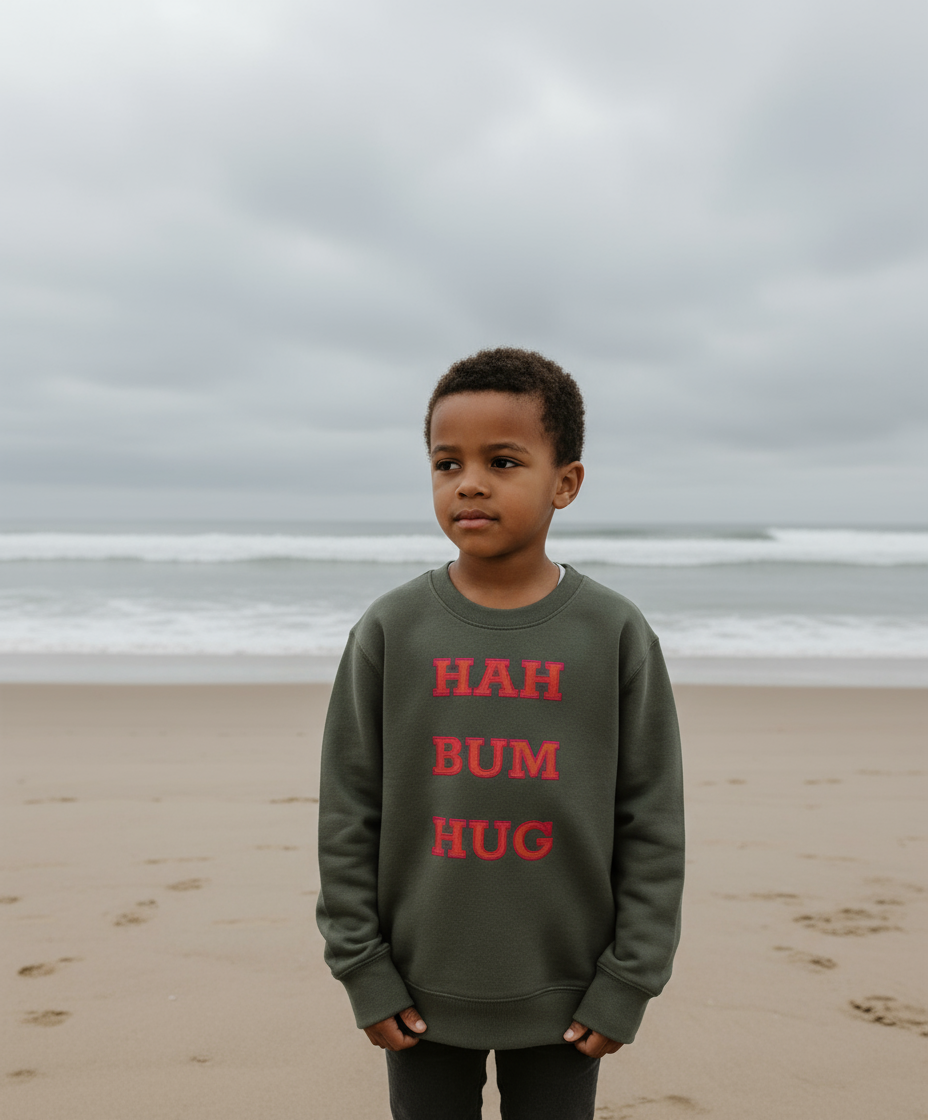 Child wearing a sweatshirt with 'HAH BUM HUG' text on a beach