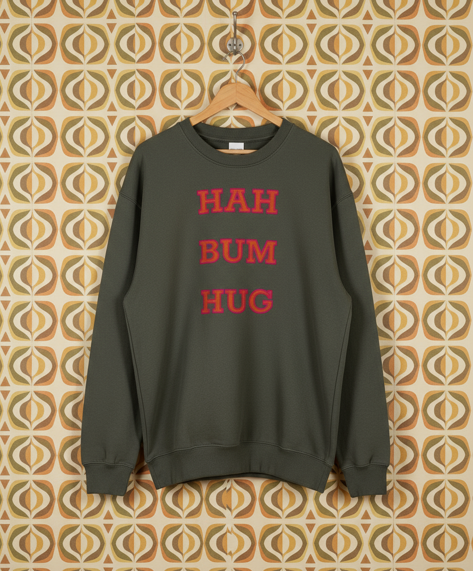 Green sweatshirt with red text 'HAH BUM HUG' on a hanger against a patterned wall.
