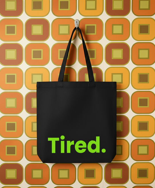 Black tote bag with 'Tired.' text on a patterned background