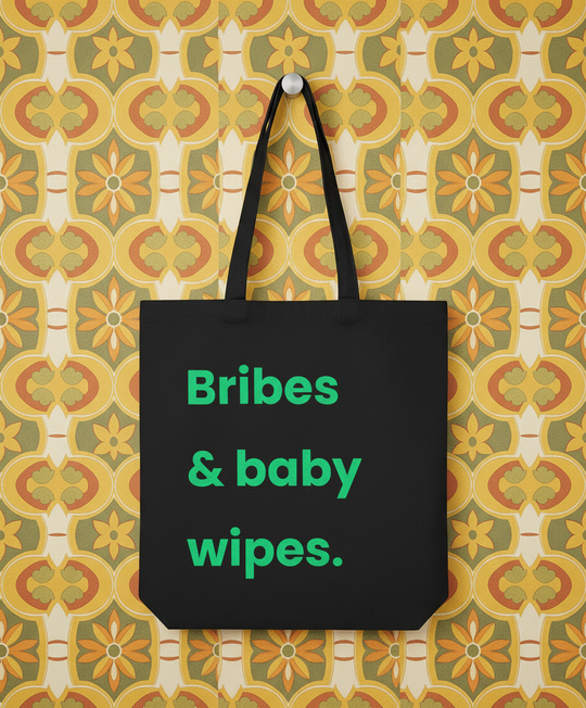 Black tote bag with green text 'Bribes & baby wipes.' on a patterned background